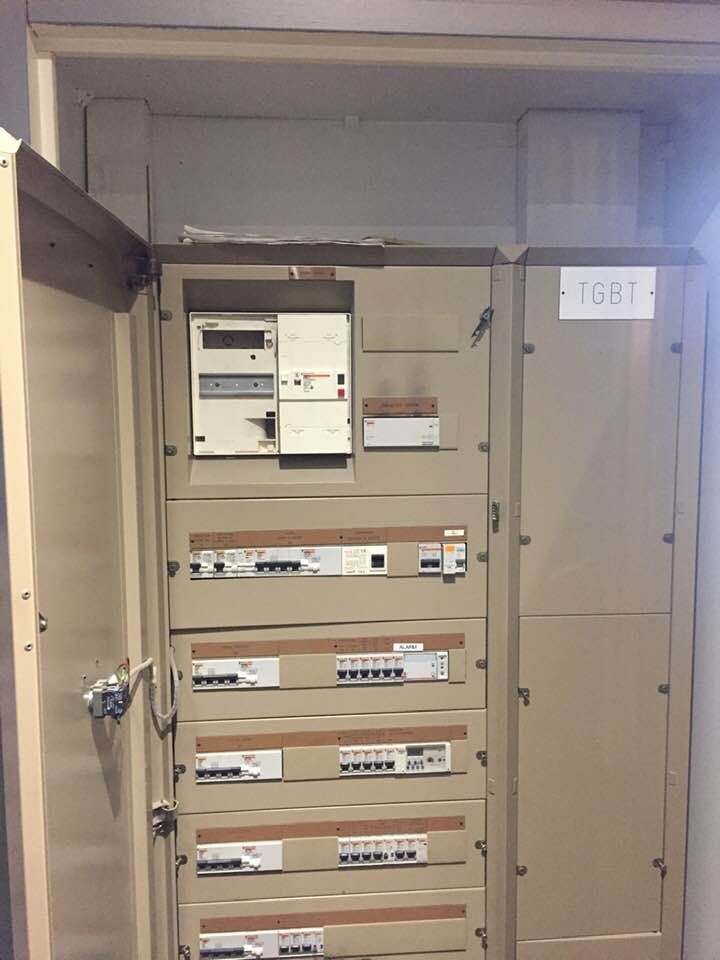 Un tableau électrique mural beige avec un compteur et plusieurs rangées de disjoncteurs à l'intérieur d'une armoire ouverte.