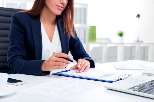 Una mujer está sentada en un escritorio con una computadora portátil y un portapapeles.