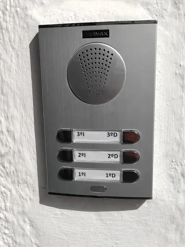 Hay un portero automático sobre una pared blanca.