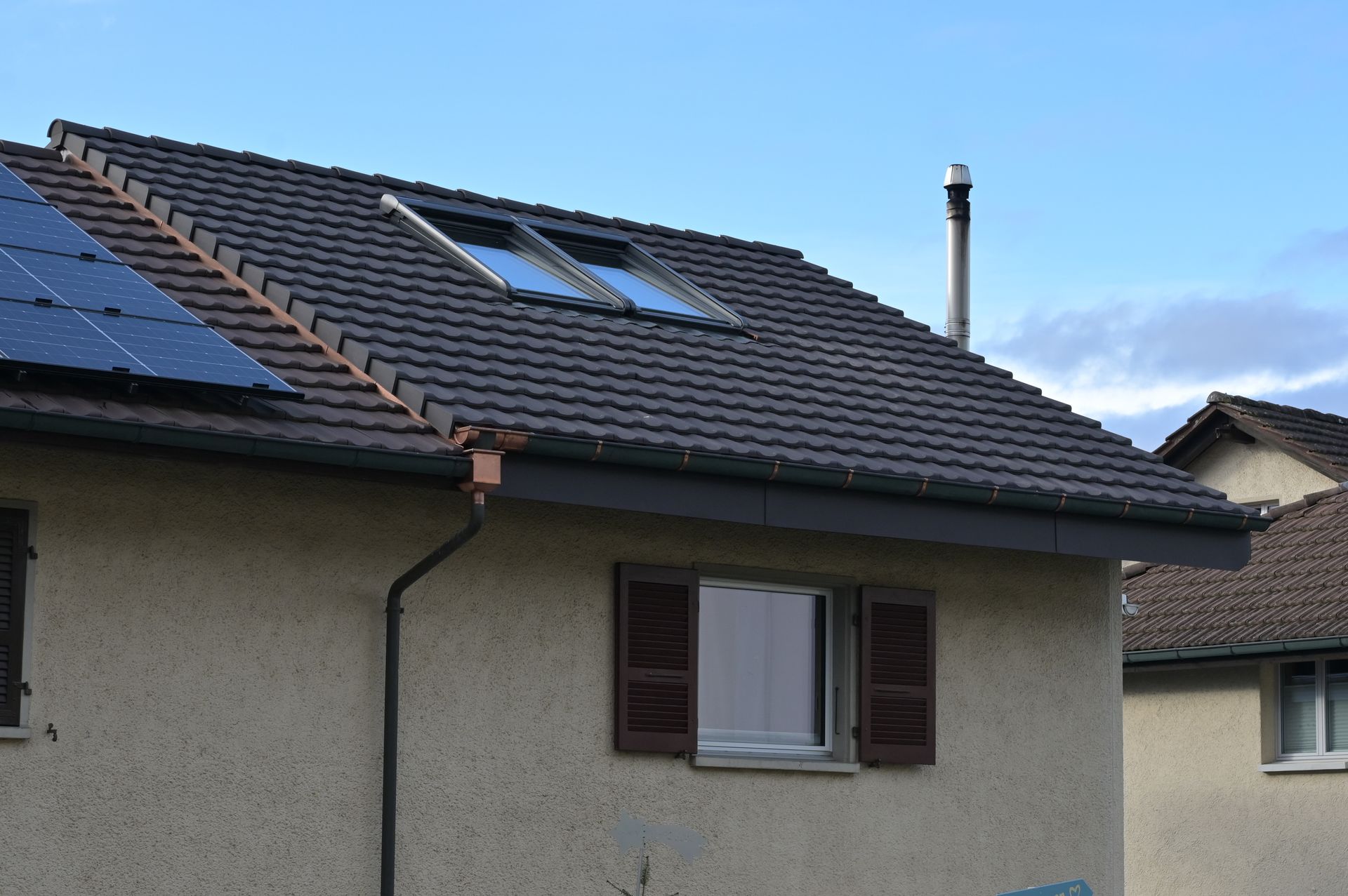 Kupferner Schornstein auf einem im Bau befindlichen Dach; im Hintergrund blaue Plane, Holzkonstruktion und grüne Bäume.