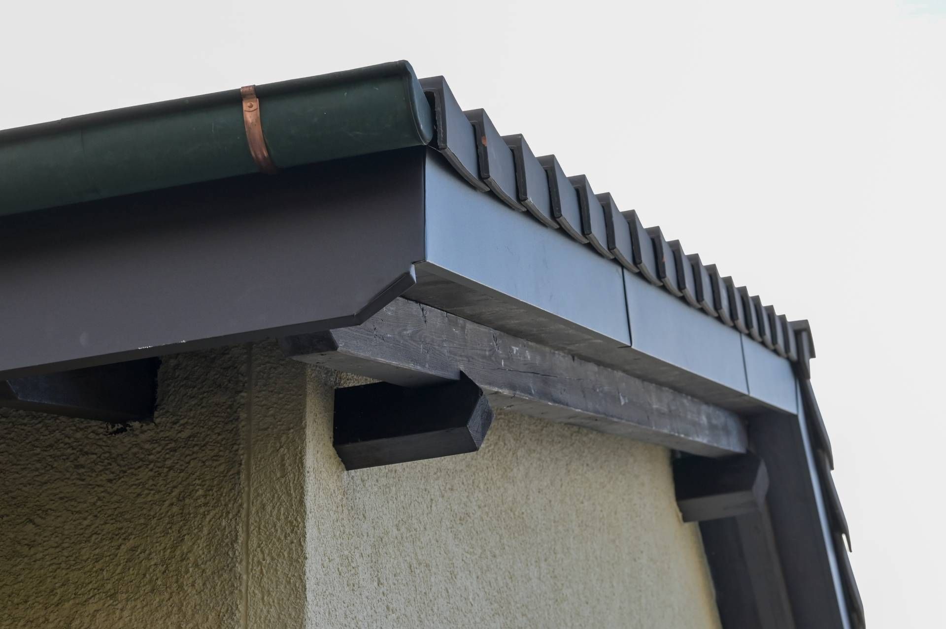Nahaufnahme eines dunkelbraunen Dachüberstands mit dekorativen Kanten und Stützbalken an einer Stuckwand.