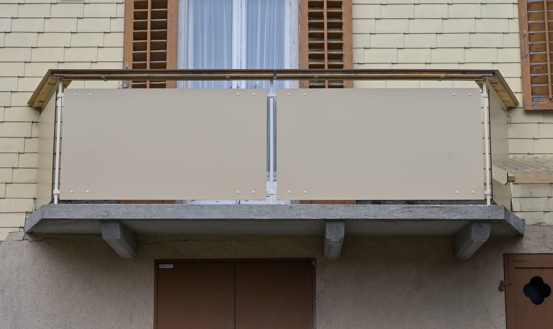 Balkon mit beigefarbenen Sichtschutzwänden, Holzgeländer, Betonsockel und beiger Gebäudefassade.