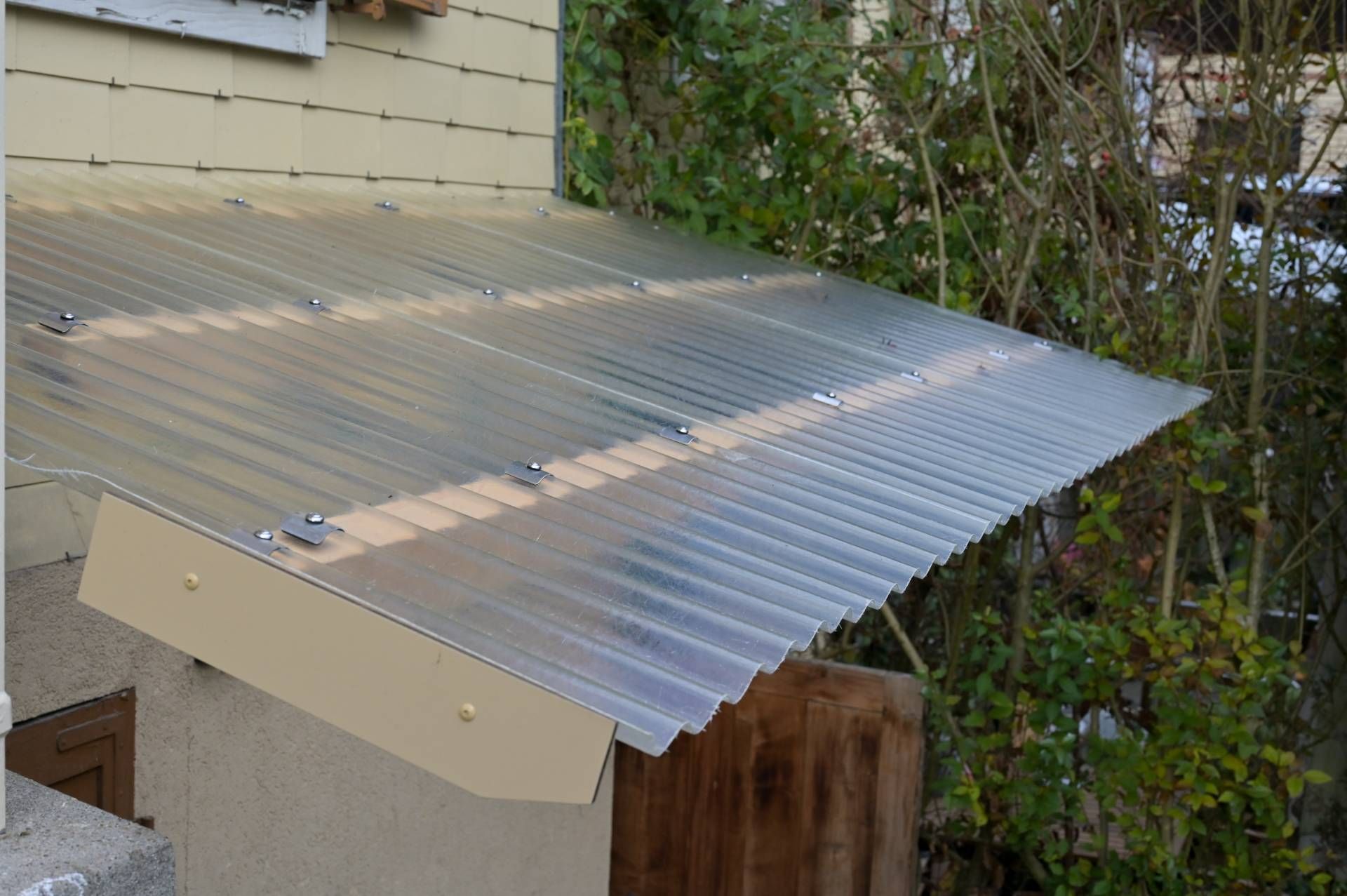 Eine durchsichtige, gewellte Kunststoffmarkise ist an einem Gebäude befestigt und bietet Schutz.