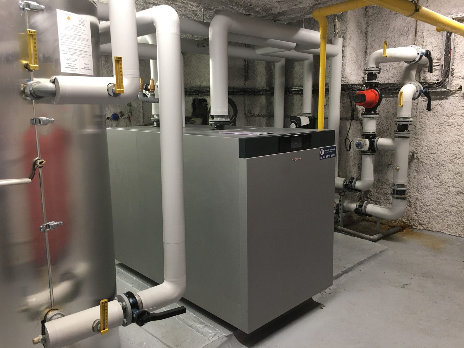 Système de chauffage avec réservoirs d'eaux grises et tuyaux isolés blancs, installé au sous-sol.