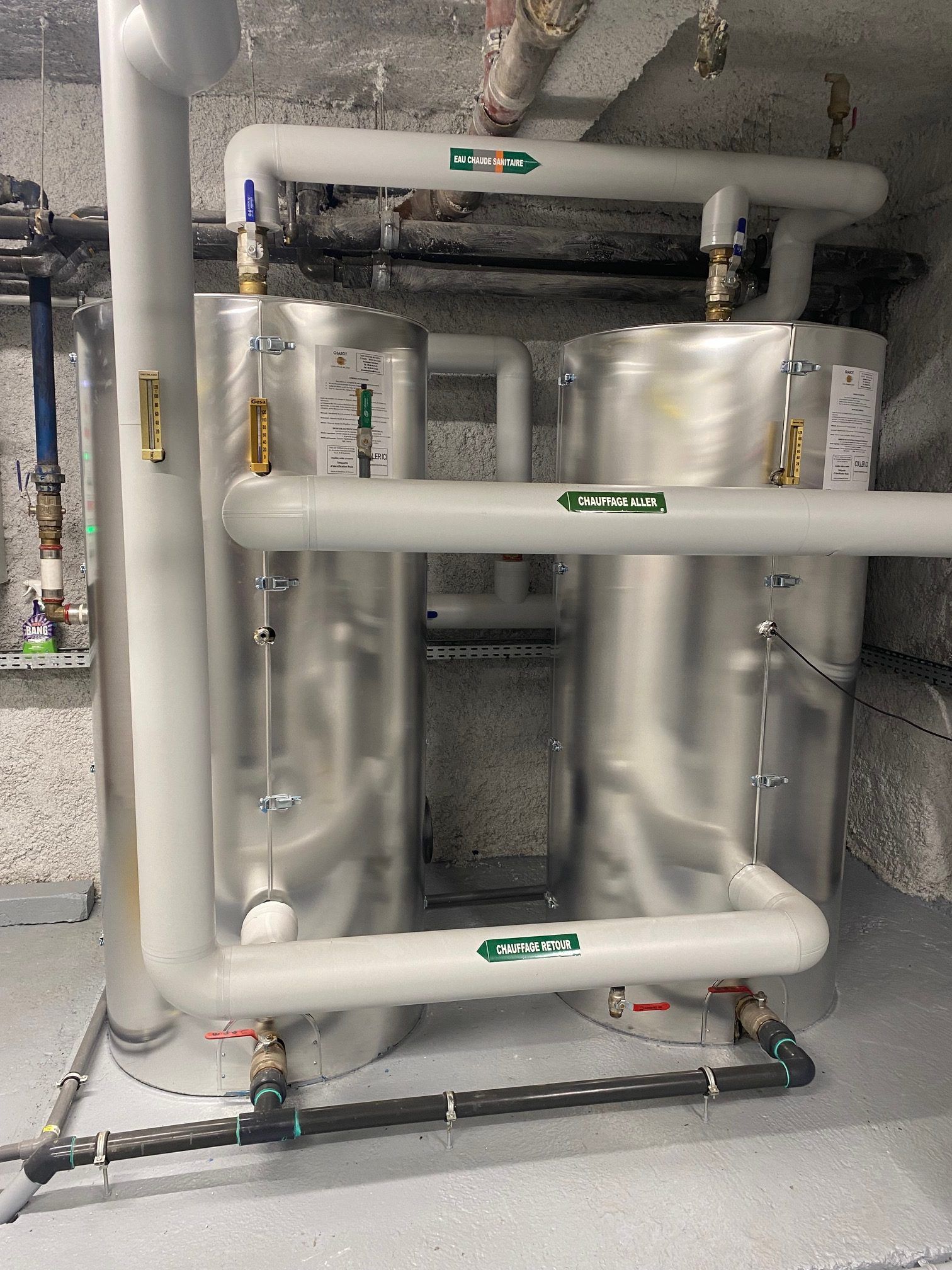 Deux réservoirs d'eau argentés avec des tuyaux blancs dans une buanderie.