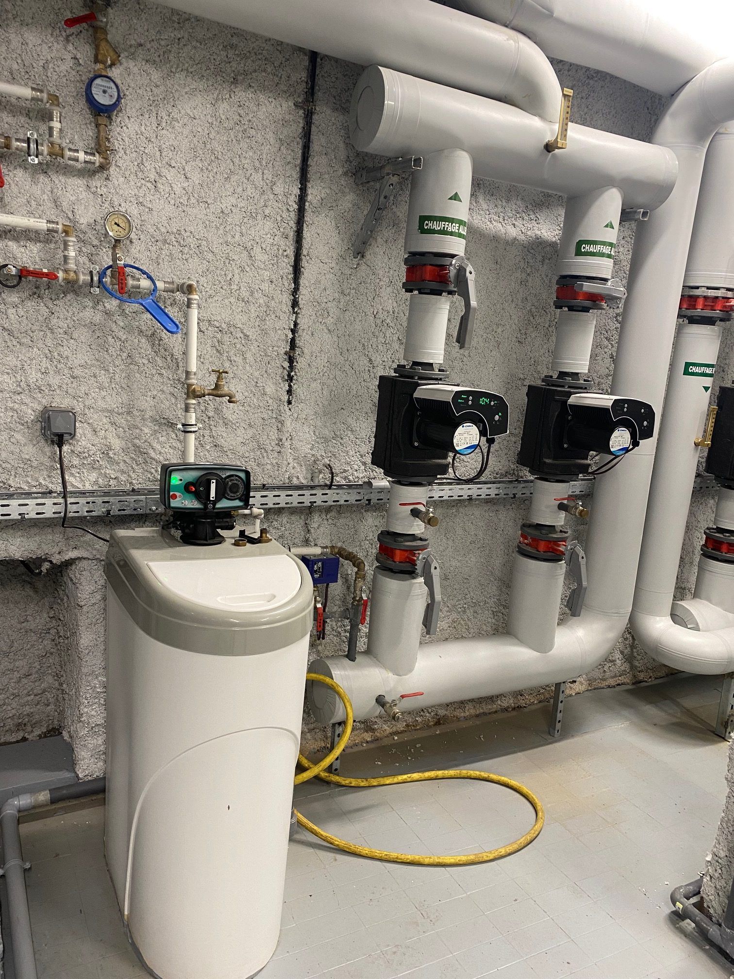 Adoucisseur d'eau à côté des tuyaux et des vannes dans une buanderie.