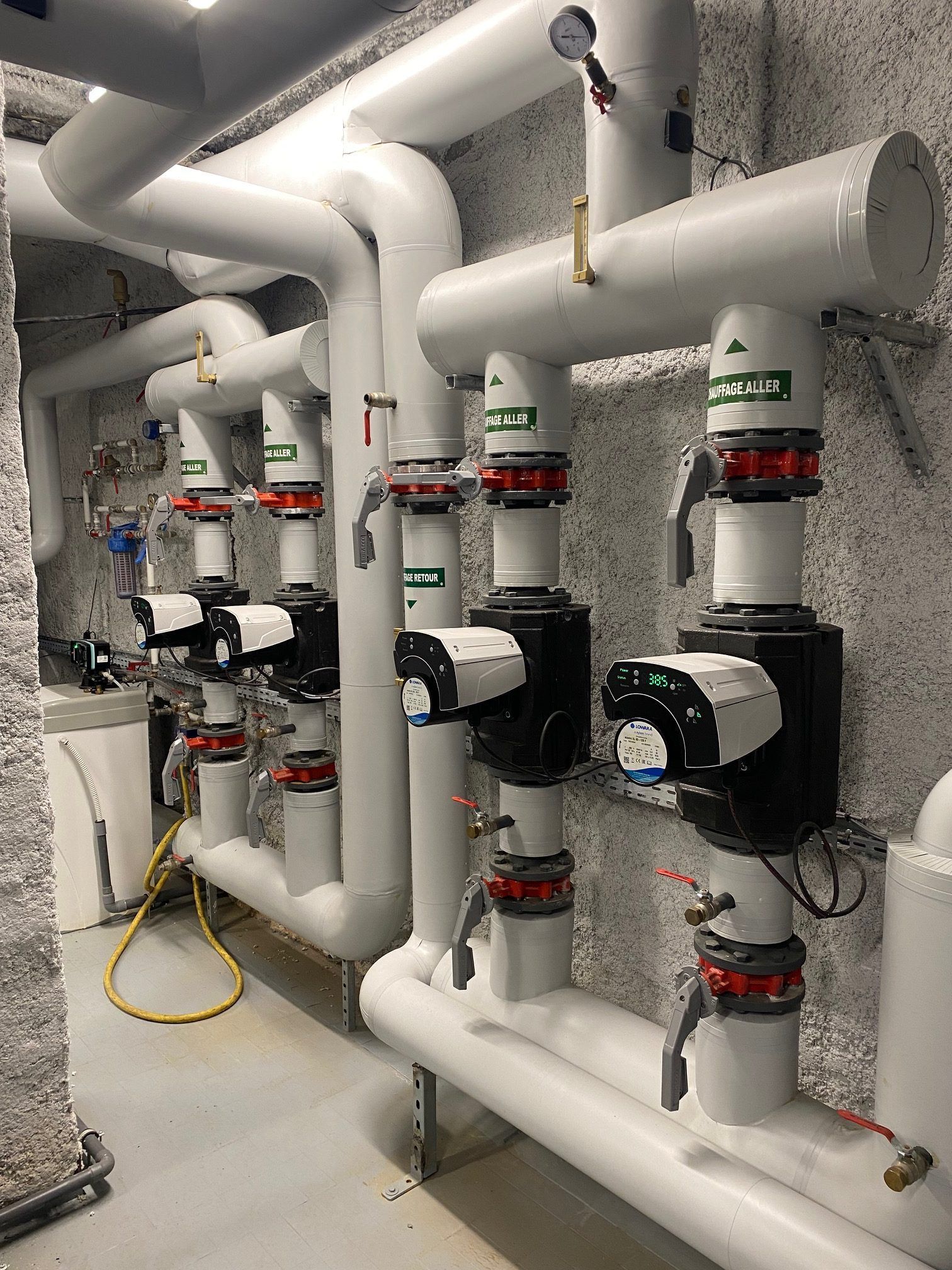 Des tuyaux blancs et des pompes noires dans un environnement industriel, probablement une salle des machines.