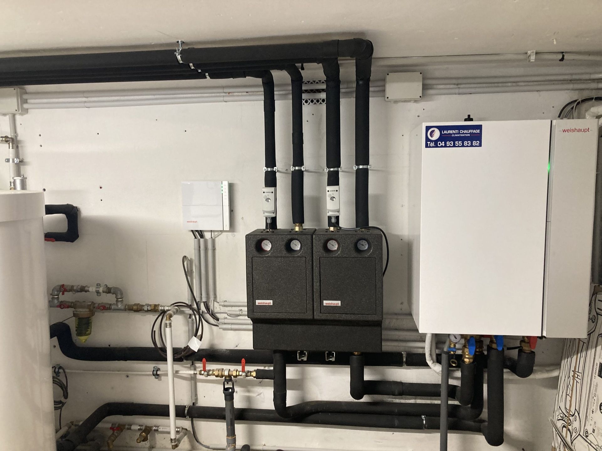 Système de chauffage avec tuyaux et panneaux contre un mur blanc dans une buanderie.