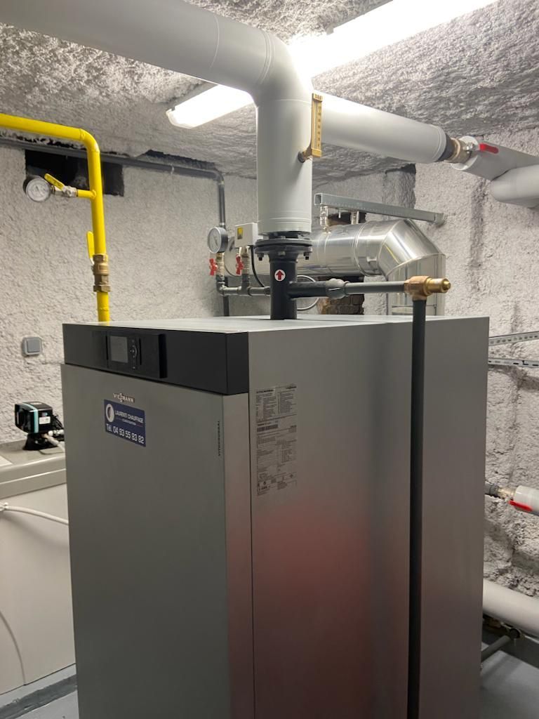 Une grande chaudière industrielle grise dans un local technique, avec des tuyaux et des manomètres.