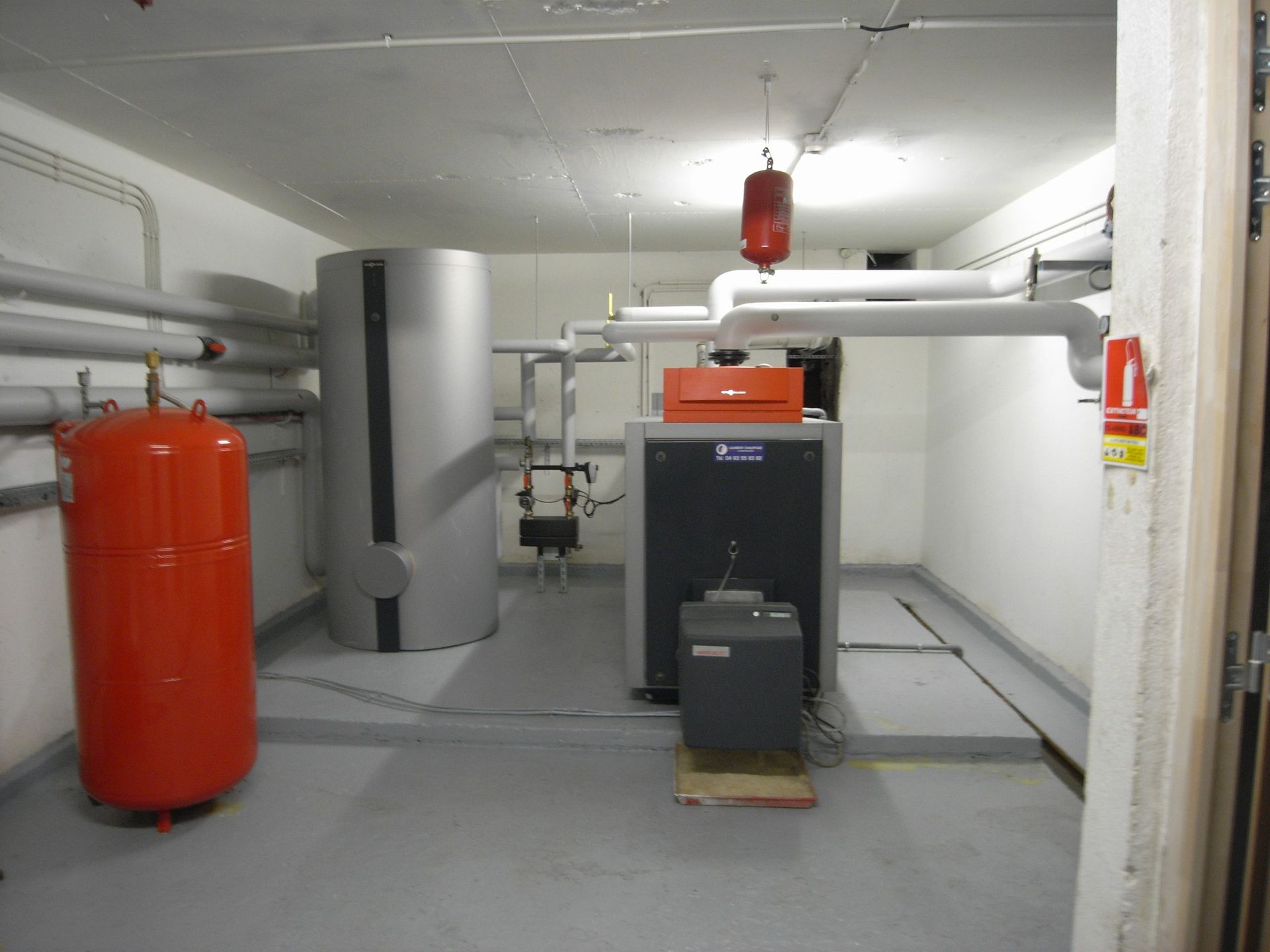 Local technique avec un grand réservoir argenté, des machines grises et des réservoirs sous pression orange.