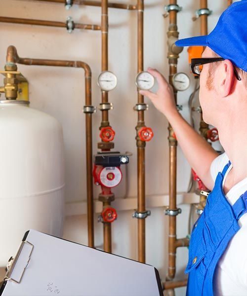 Un plombier en salopette bleue vérifie les manomètres des tuyaux, un bloc-notes à la main, dans la buanderie.
