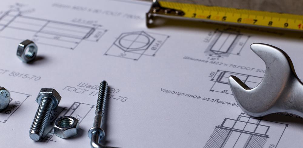Gros plan sur des plans techniques montrant des boulons, une clé et un mètre ruban.