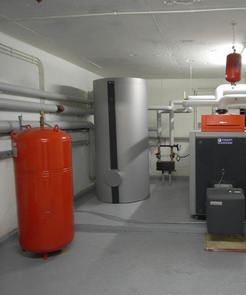 Réservoirs et tuyaux industriels rouges et gris dans un local technique.