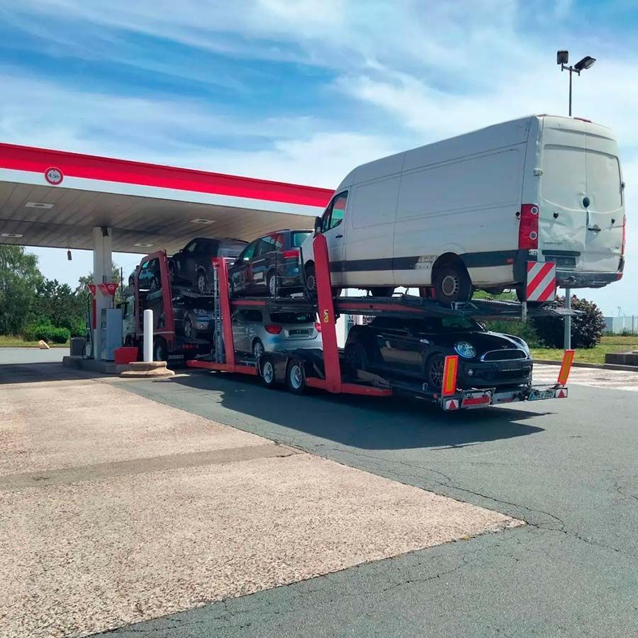 Un camión que transporta coches está aparcado delante de una gasolinera.