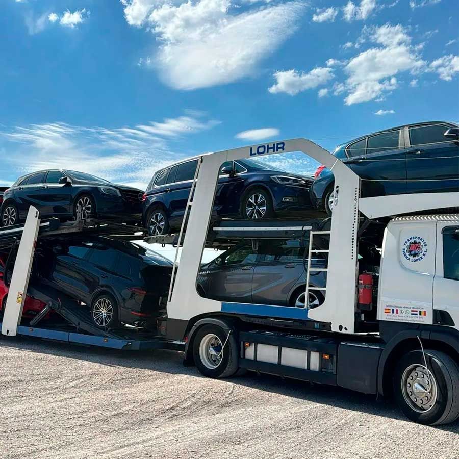 Un camión loria transporta un montón de coches por un camino de grava.