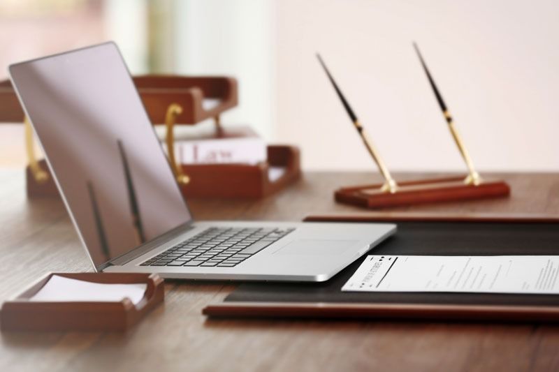 Computadora portátil, papeles y bolígrafos sobre un escritorio de madera en un entorno de oficina.