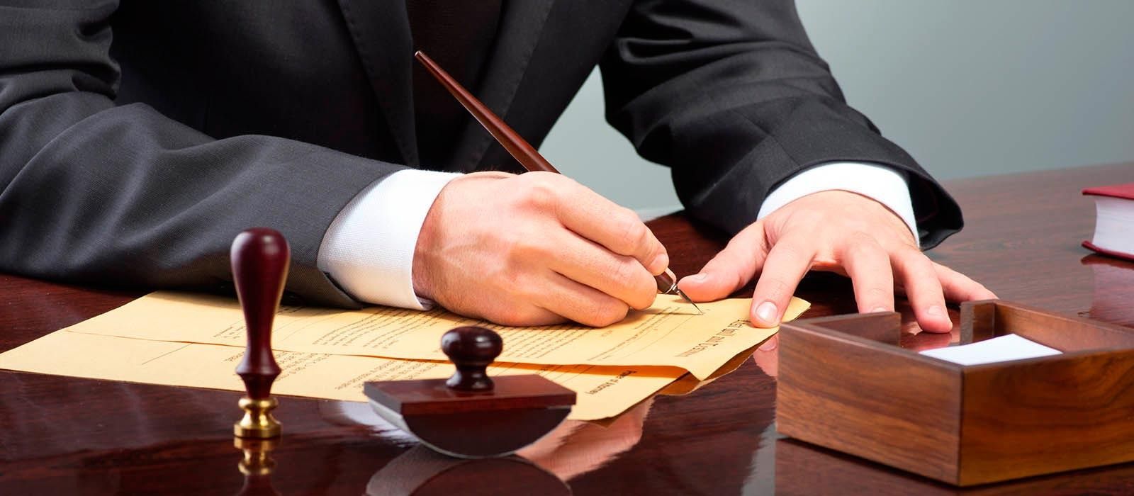Una persona con traje firma un documento con pluma en un escritorio. Vista de cerca.