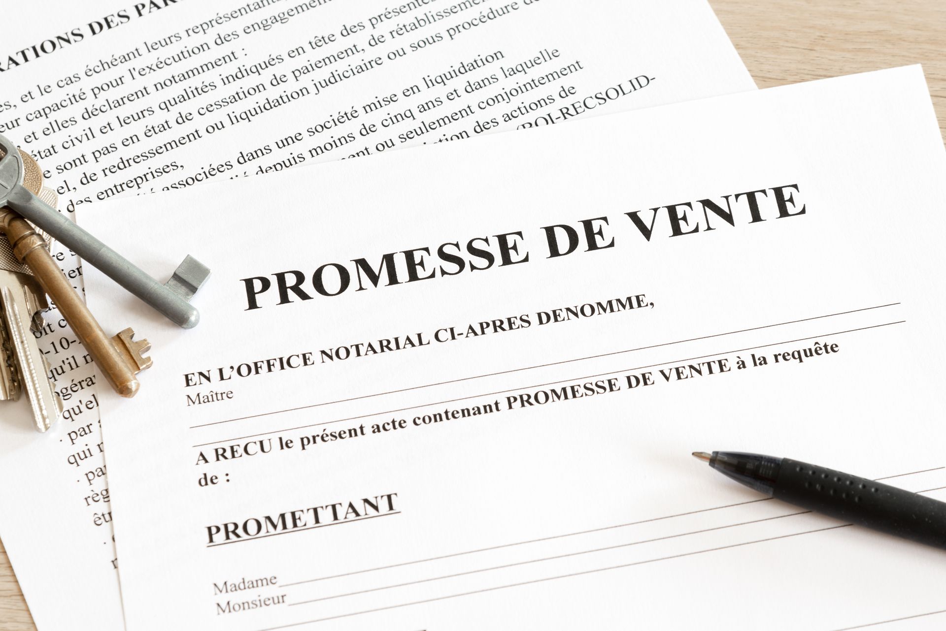 Un document de promesse de vente (contrat de vente) posé sur un bureau à côté d'une clé en métal et d'un stylo noir.