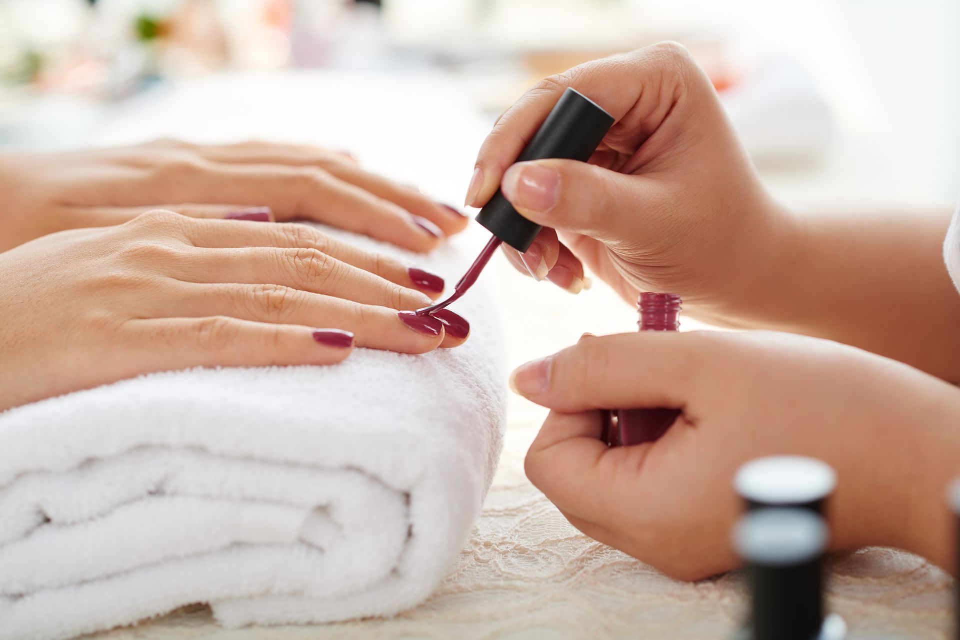 Une manucure applique du vernis à ongles rouge sur les ongles d'une cliente, sur une serviette blanche.