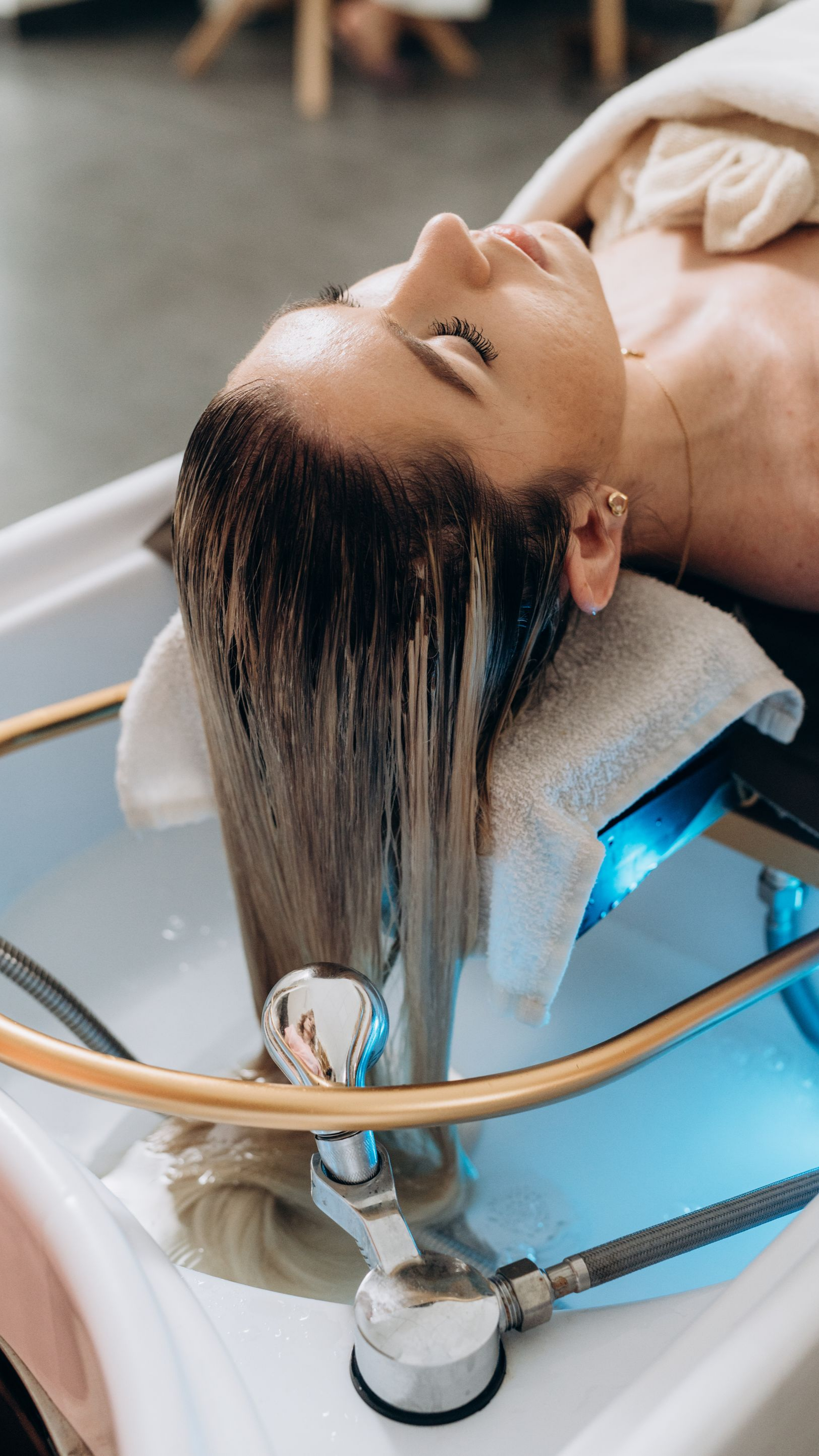 Personne aux cheveux blonds mouillés, se faisant laver les cheveux dans un lavabo de salon.