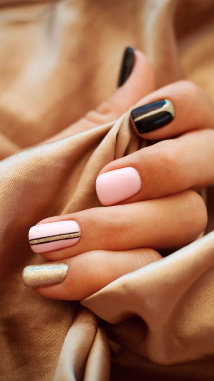 Main avec une manucure aux ongles roses, dorés et noirs sur un fond en tissu beige.