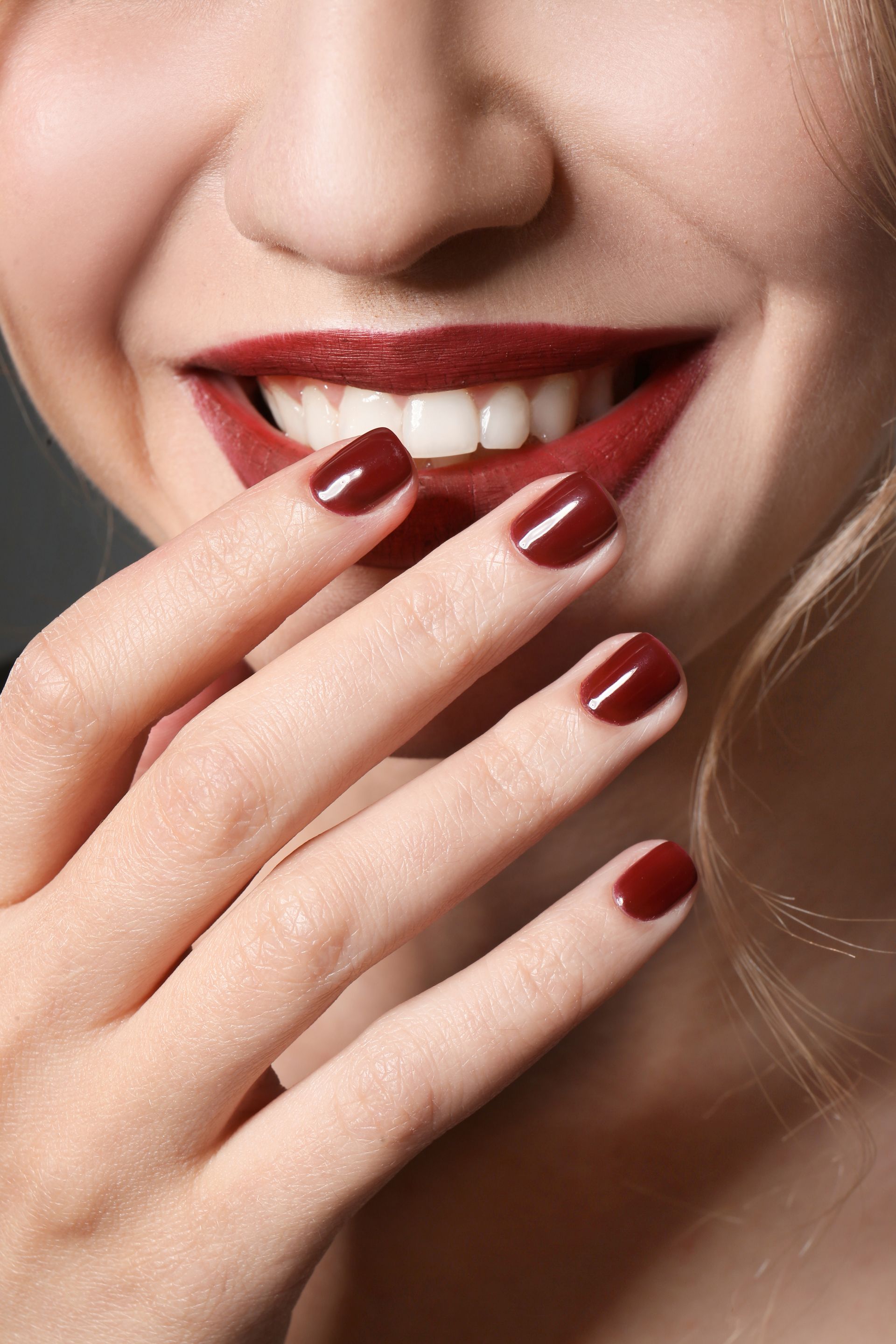 Personne souriante avec du rouge à lèvres rouge et du vernis à ongles assorti.