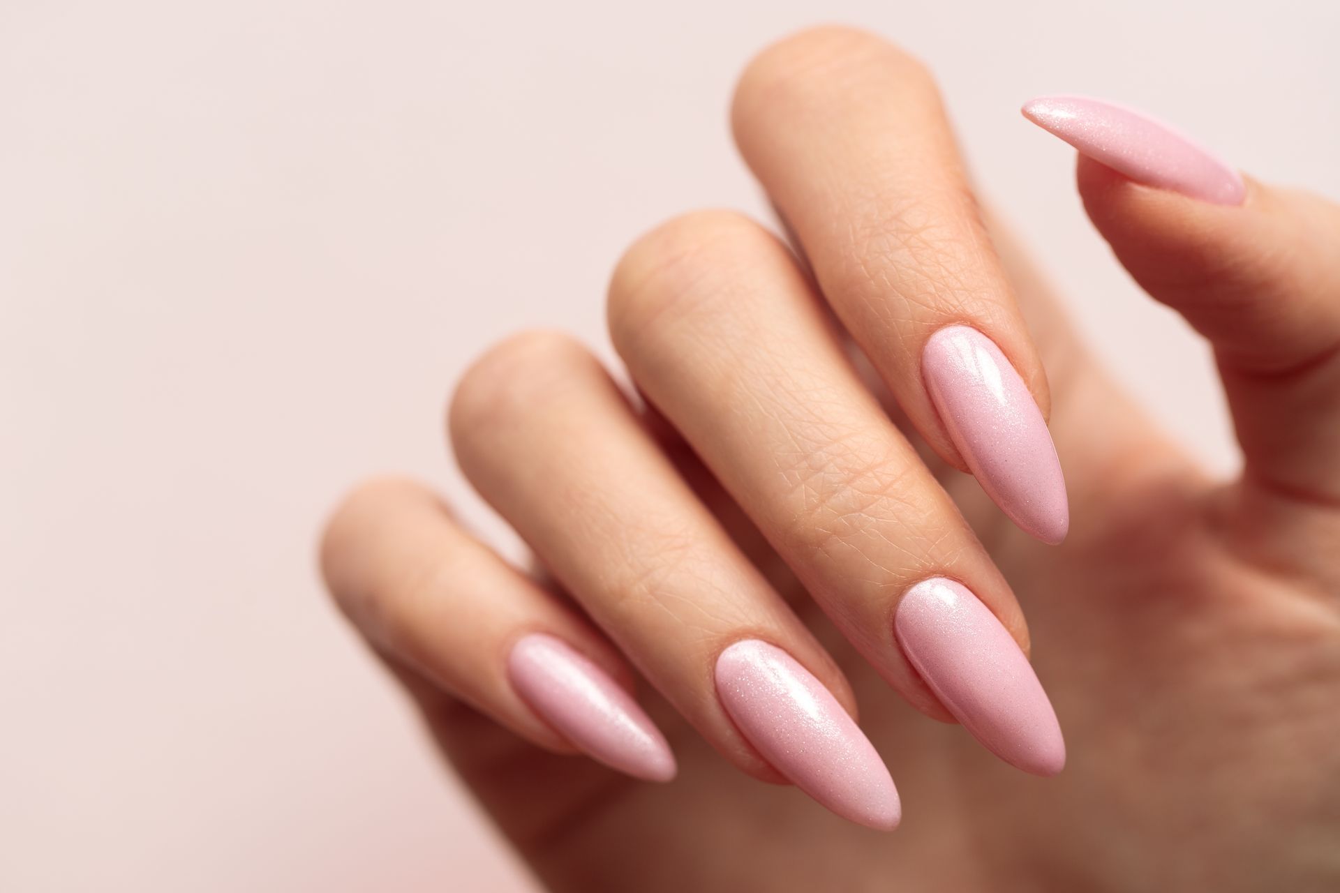 Main aux ongles longs, pointus et vernis d'un rose clair.