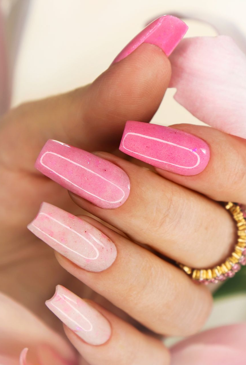 Main aux longs ongles en acrylique roses, tenant des fleurs roses et une bague en or.