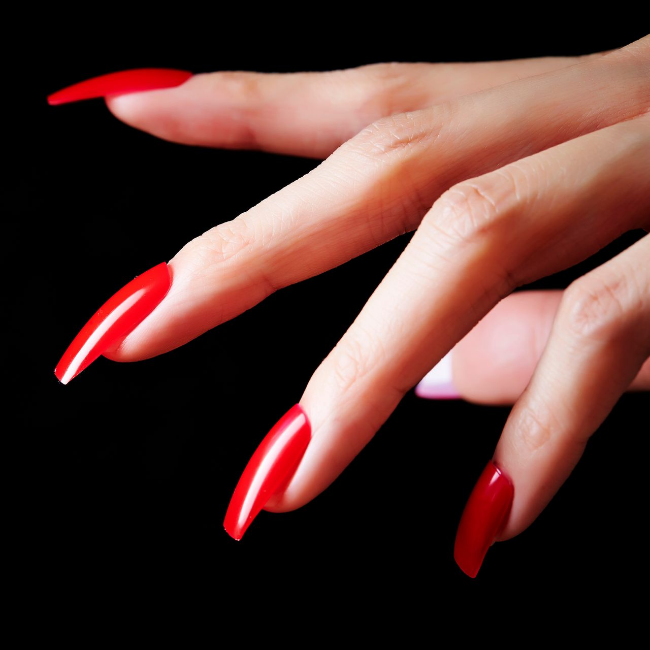 Des mains aux longs ongles rouges et brillants sur fond noir.