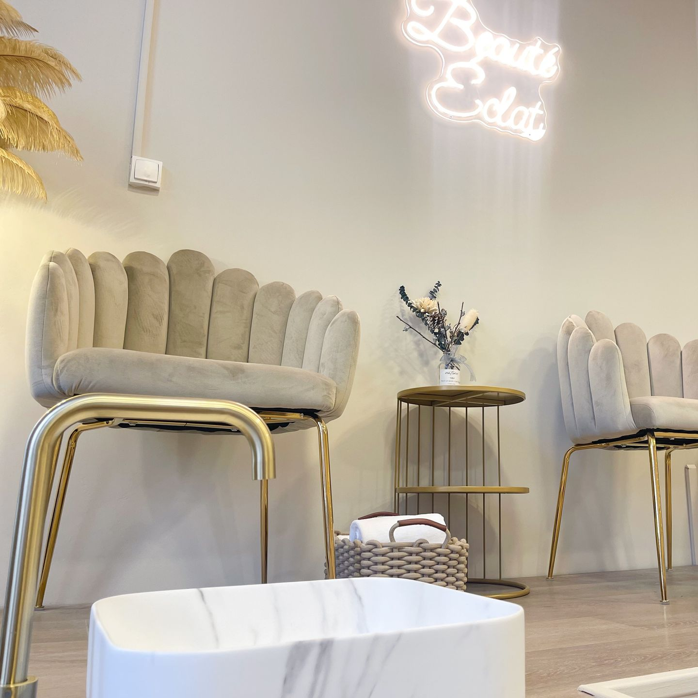 Intérieur d'un salon de manucure avec deux fauteuils en forme de coquillage, une petite table et un bac à pédicure. Éclairage tamisé, tons neutres.