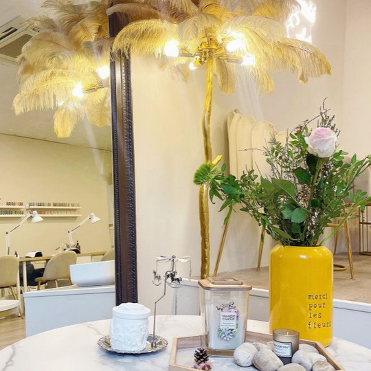 Photo intérieure d'un salon de manucure avec un miroir, une décoration florale et un luminaire doré en forme de palmier.