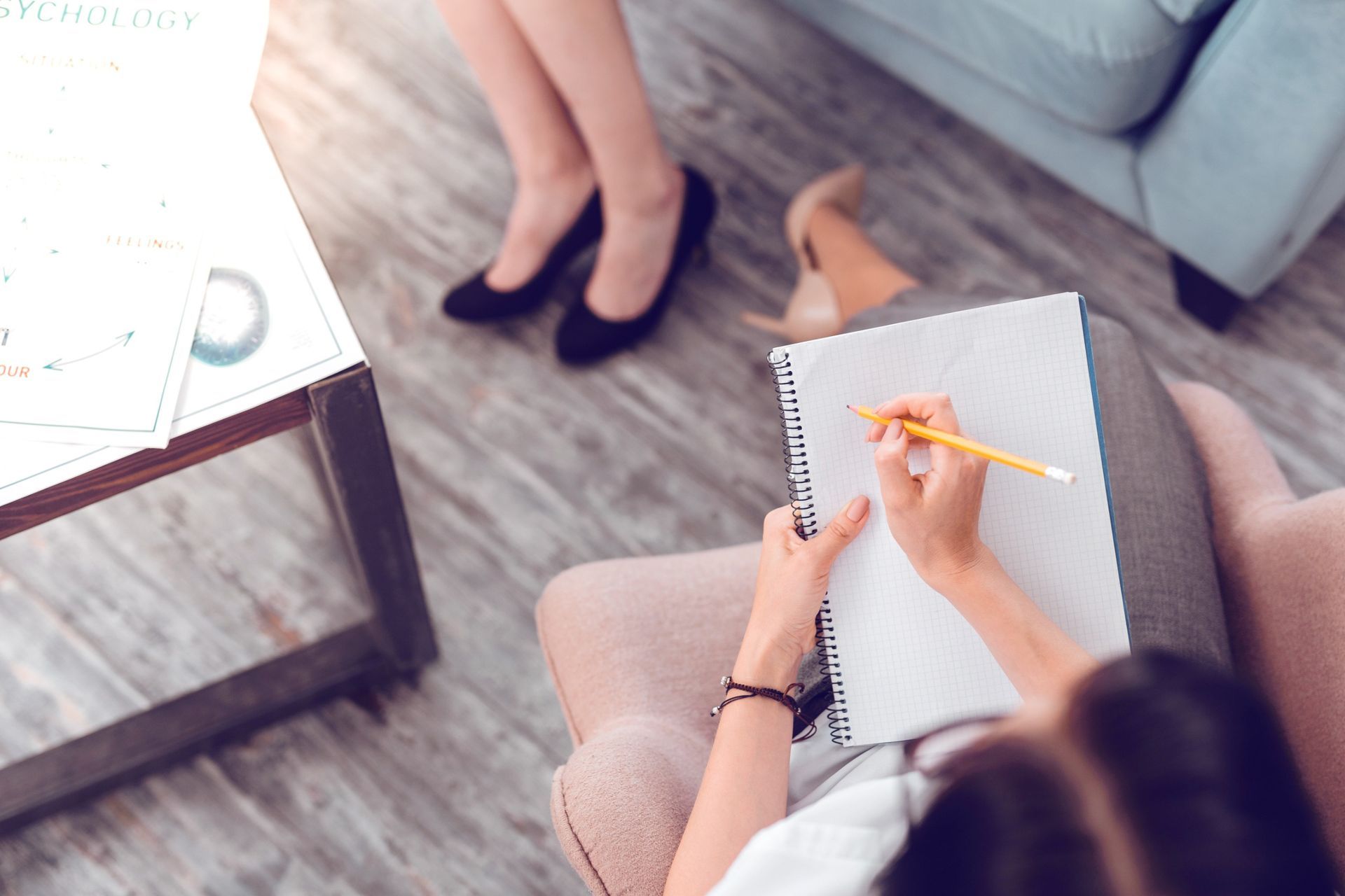 Una mujer está sentada en una silla escribiendo en un cuaderno con un lápiz.