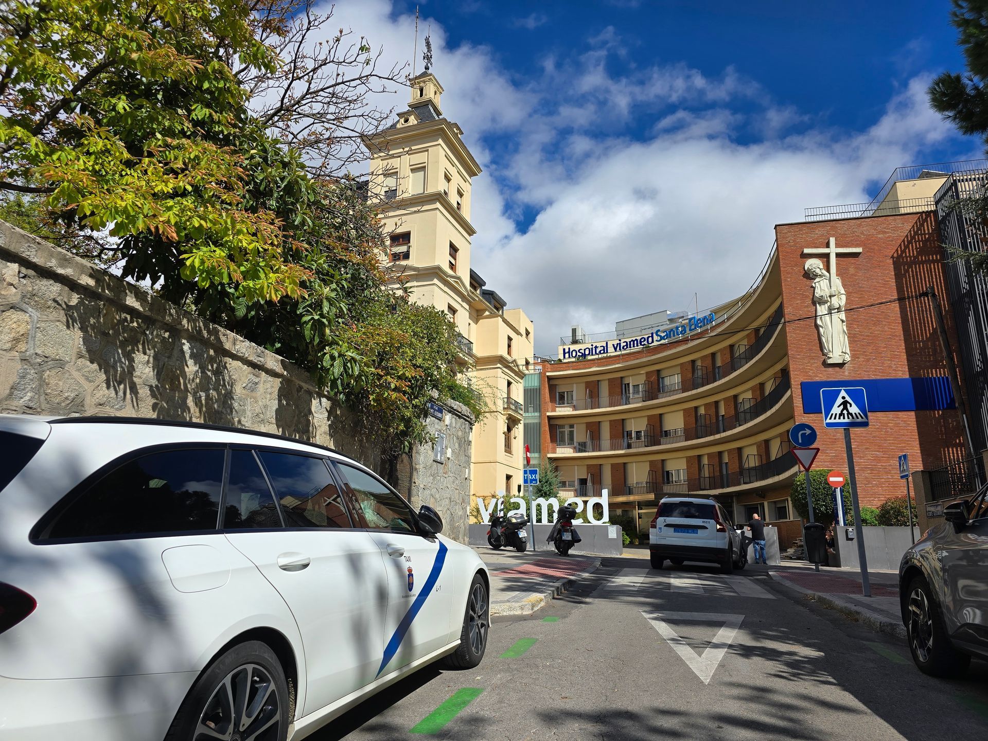 Calle curva de la ciudad con taxi Jesús Picas aparcado, una señal azul para peatones y Hospital Santa Elena de fondo