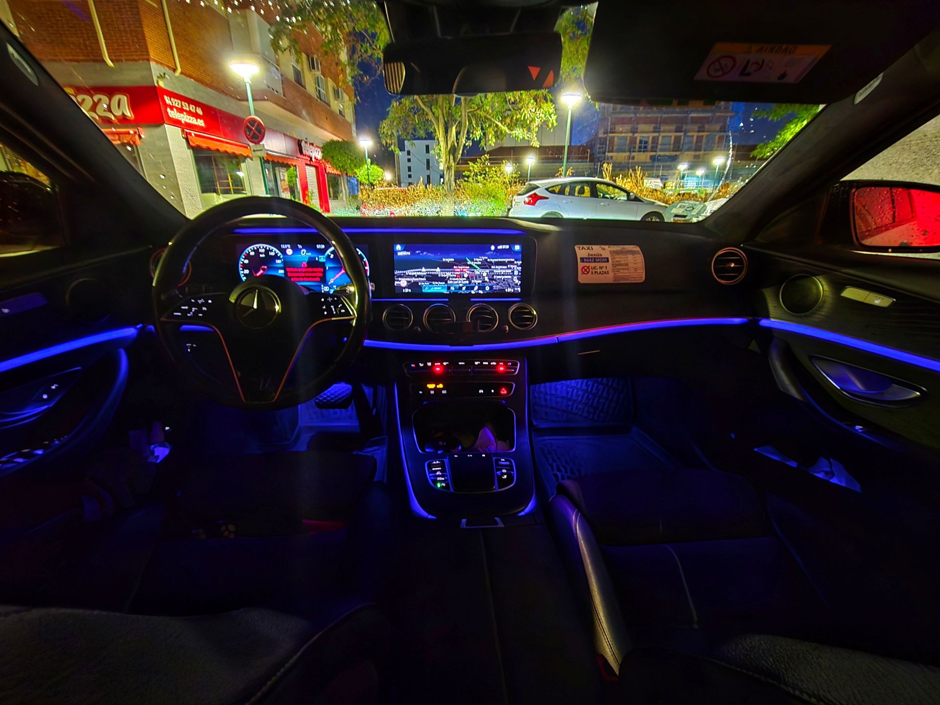 Interior del taxi Mercedes Benz Jesús Picas con iluminación ambiental azul. El tablero tiene una pantalla digital y la escena es al aire libre, de noche.
