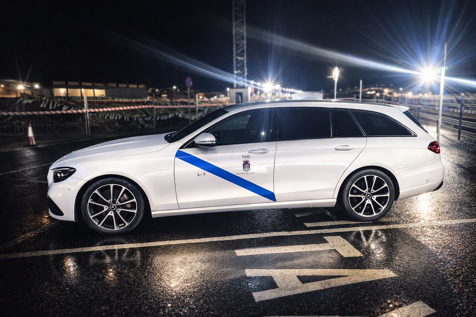 Taxi Mercedes Blanco de Navalmoral de la Mata estacionado de noche en una parada de taxis sobre suelo mojado
