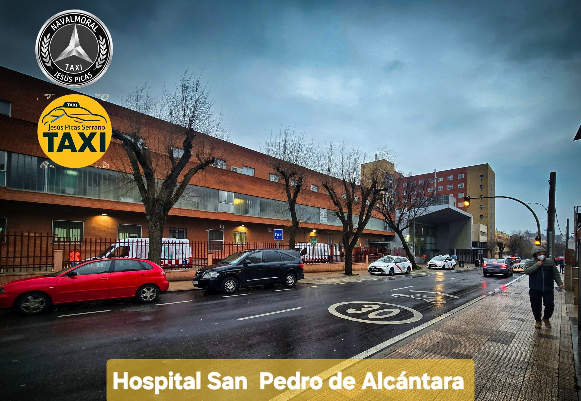 Entrada del Hospital San Pedro de Alcántara en una calle mojada con coches, taxis y peatones cerca.