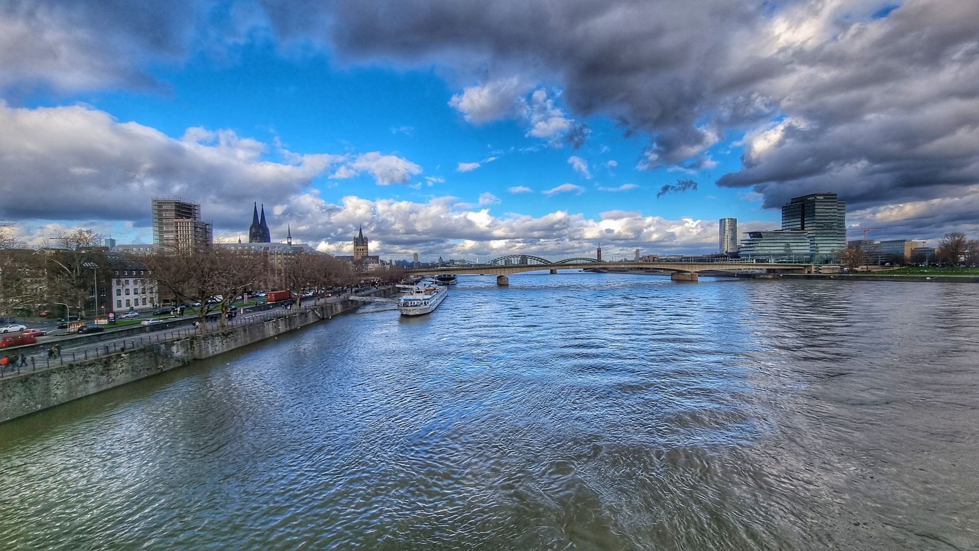 Vista panorámica de la ciudad Coloniabajo un cielo azul nublado, con puentes y edificios a lo largo del agua.