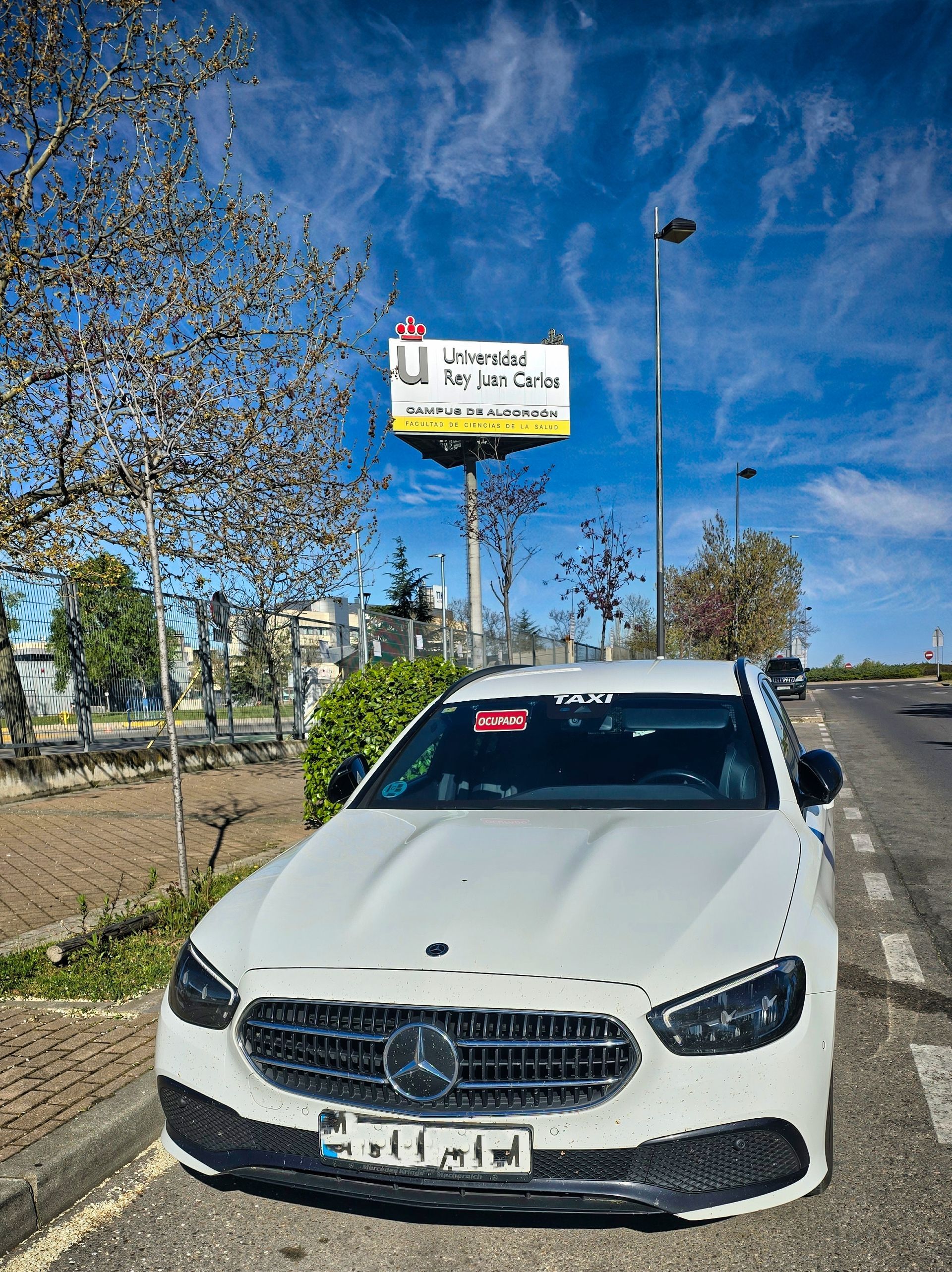 Taxi Mercedes de Jesús Picas de Navalmoral de la Mata cerca de un cartel de la Universidad Juan Carlos I de Alcorcón, Madrid