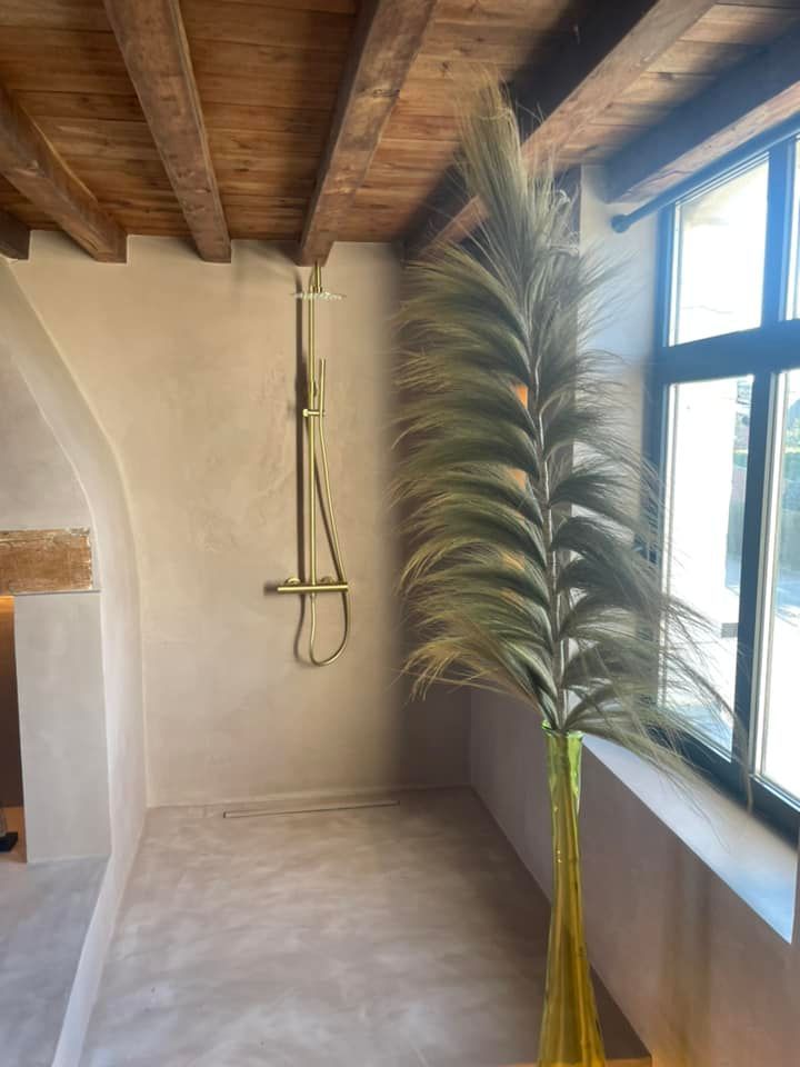 Un pommeau de douche doré accroché à un mur de pierre et une fenêtre qui éclaire la pièce