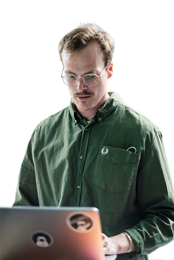 Mann mit Brille und Schnurrbart, der an einem Laptop arbeitet und ein grünes Hemd mit Knöpfen trägt.