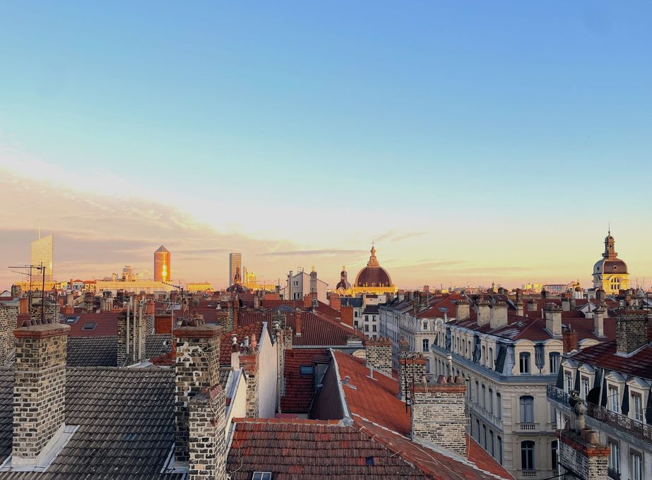 Panorama urbain au crépuscule, avec ses toits historiques et sa tour de cathédrale imposante.