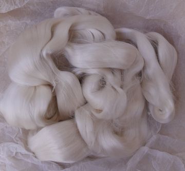Des mains tissent des fils sur un métier à tisser dans une lumière chaude et tamisée.