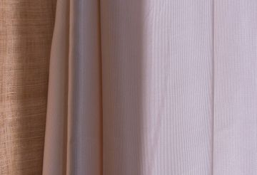 Des mains tenant une écharpe à motifs colorés nouée sur la poitrine par-dessus une chemise à rayures.