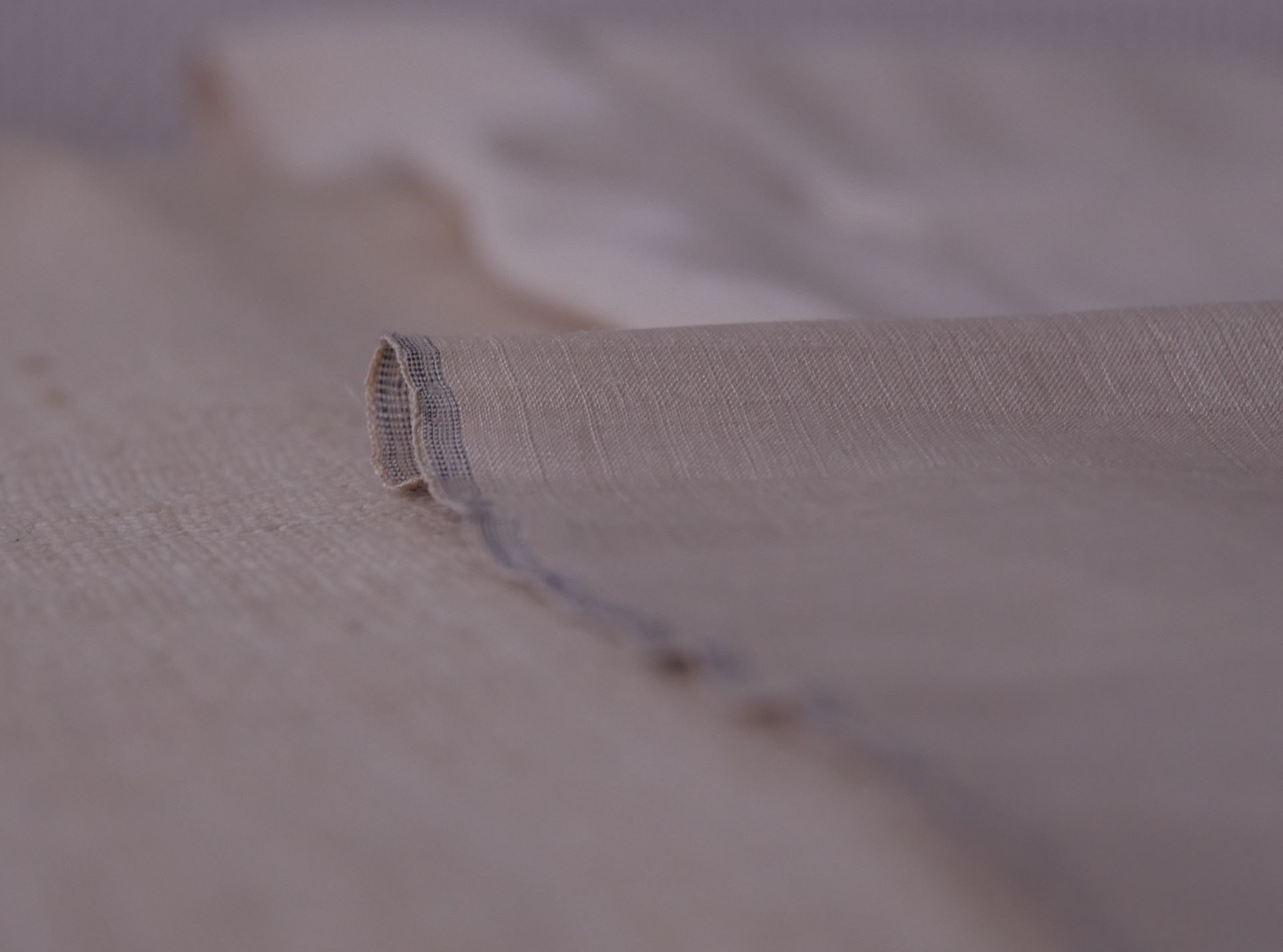 Gros plan sur un tissu satiné beige doux aux plis fluides et au motif texturé subtil.