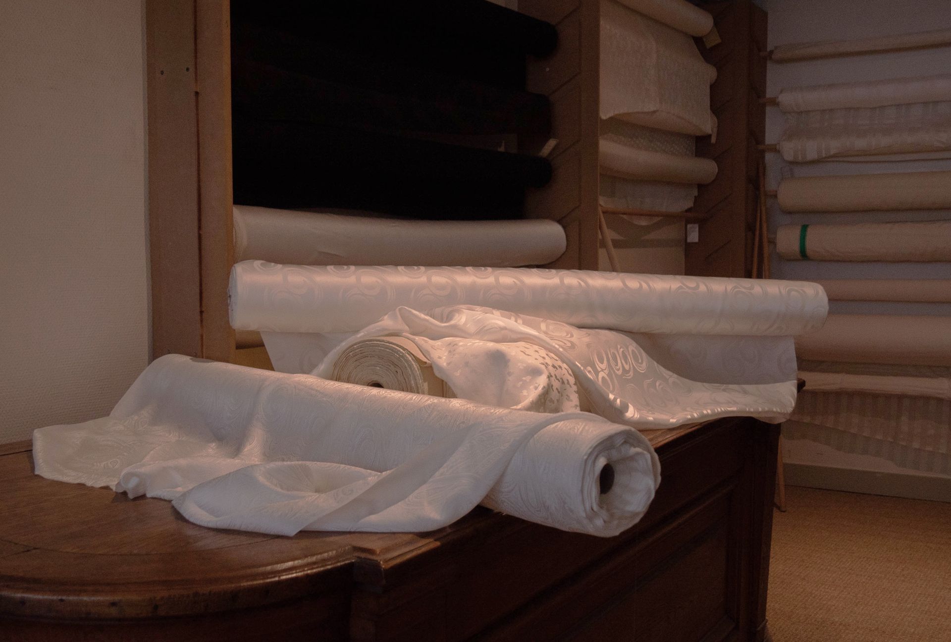 Robe de mariée blanche soutenue par deux personnes dans une cabine d'essayage à la lumière tamisée.