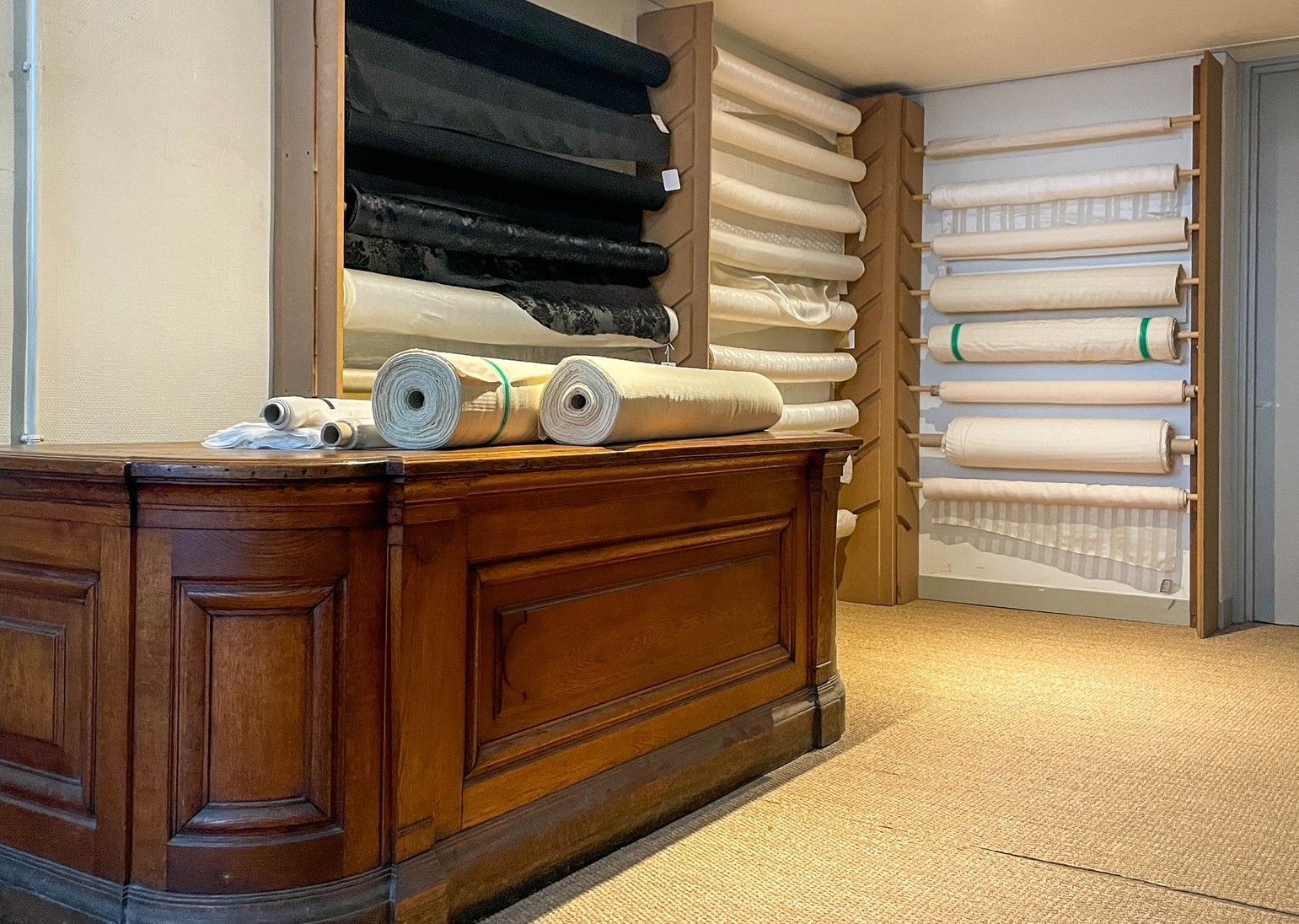 Comptoir en bois à côté d'étagères remplies de tapis pliés et de rouleaux de tissu.
