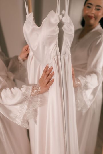 Robe de mariée blanche soutenue par deux personnes dans une cabine d'essayage à la lumière tamisée.