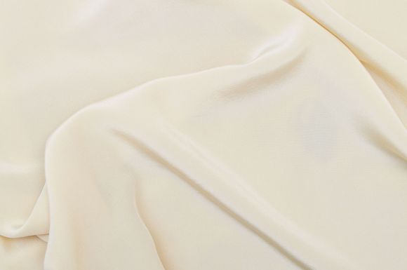 Gros plan sur un tissu couleur crème aux plis souples et à la texture tissée subtile.