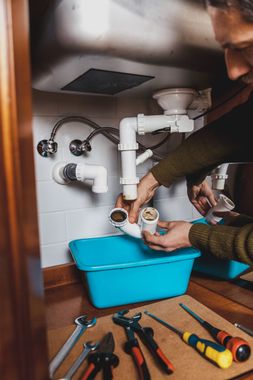 Un hombre está arreglando un fregadero en una cocina.