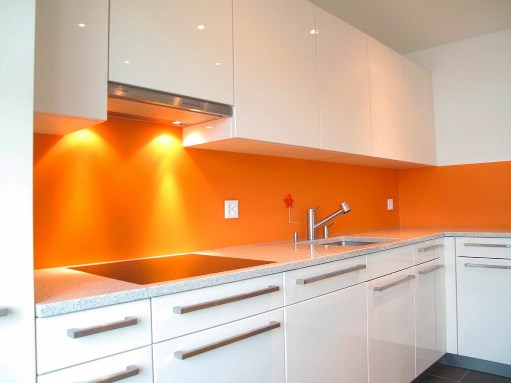 Moderne Küche mit weissen Schränken, Edelstahlbeschlägen, orangefarbenem Fliesenspiegel und Einbauleuchten.